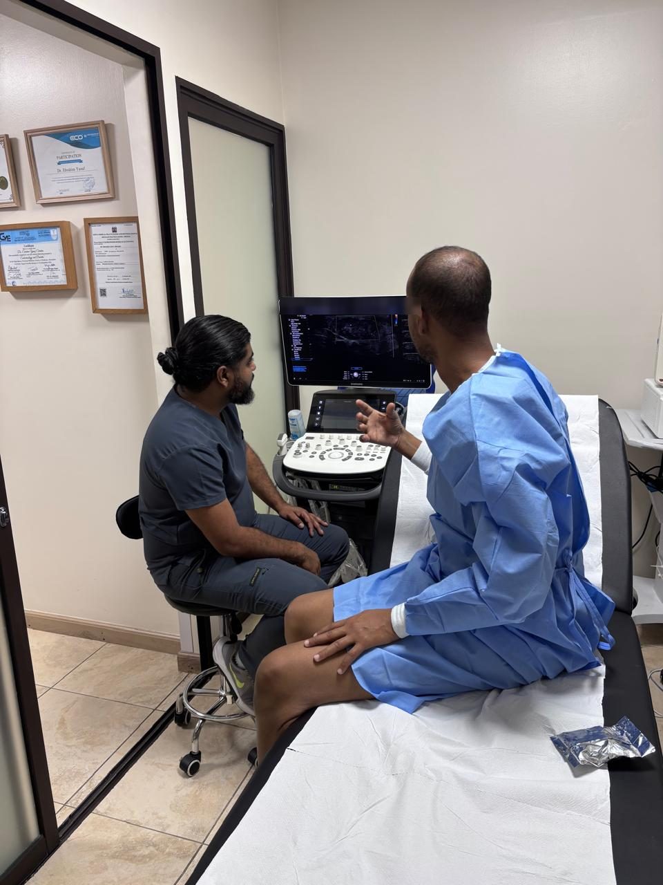 After thyroid RFA — the patient sits up in a gown and discusses the ultrasound images with Dr. Ebrahim Yusuf (screen details hidden; shared with written consent)